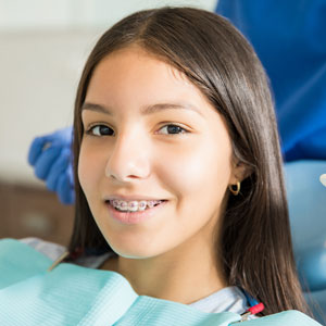 Close-up portrait of smiling teenage girl with braces against dentist standing in clinic