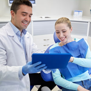 Happy male dentist showing tablet pc computer to woman patient at dental clinic office